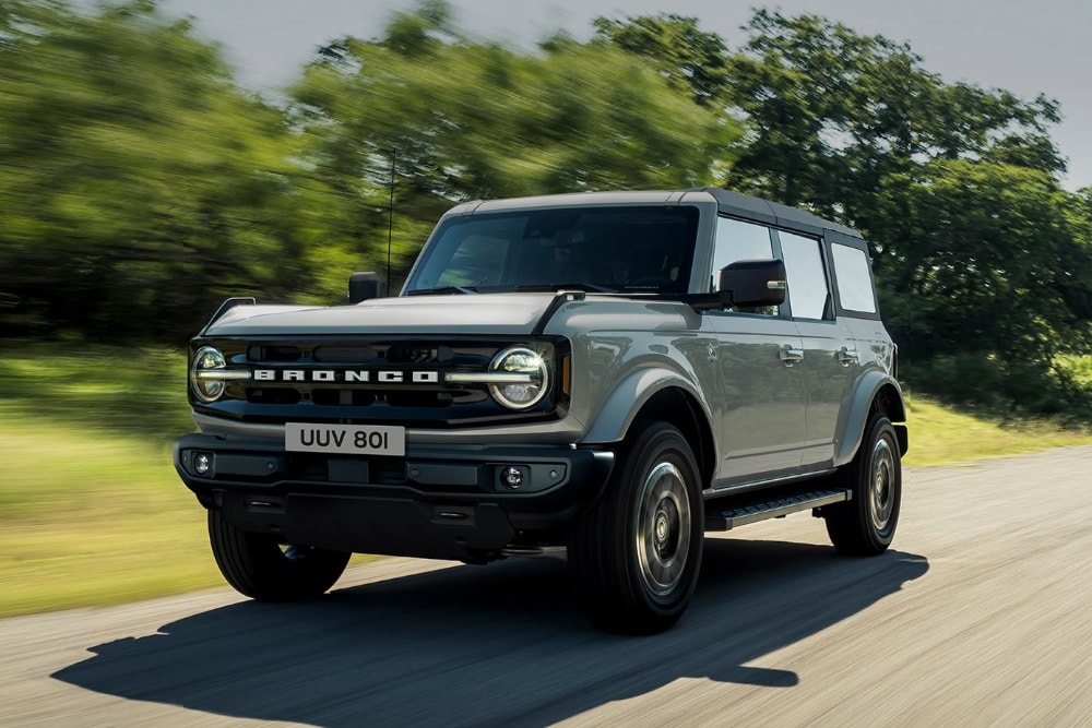 Front view of a blue Ford Bronco driving on a dirt road. 
