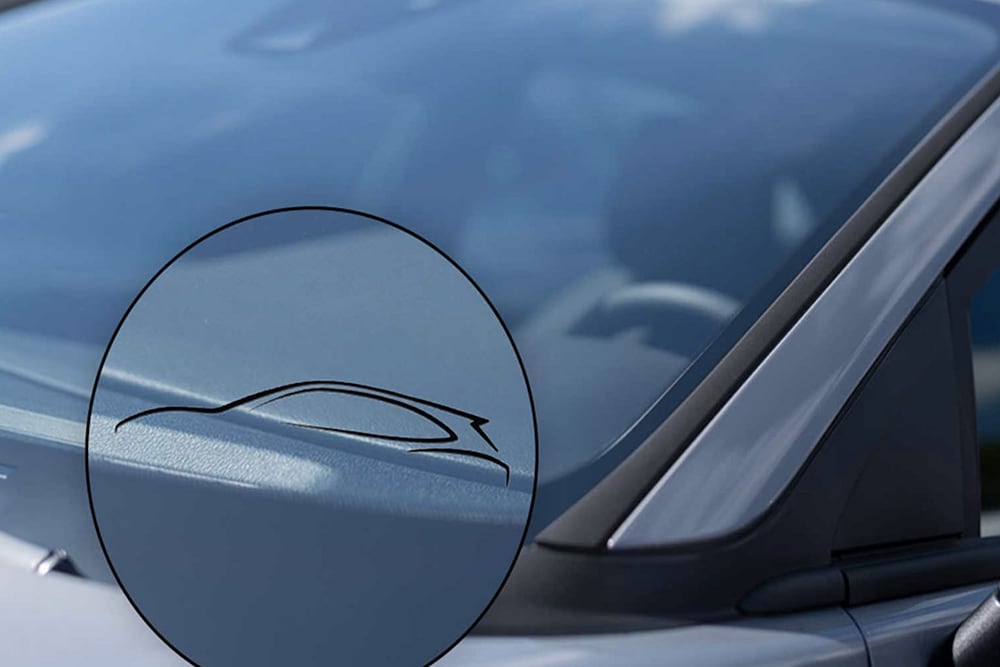  Zoom sur un pare-brise de voiture Ford avec le symbole d’un pare-brise certifié d’origine, visible à travers une loupe graphique.