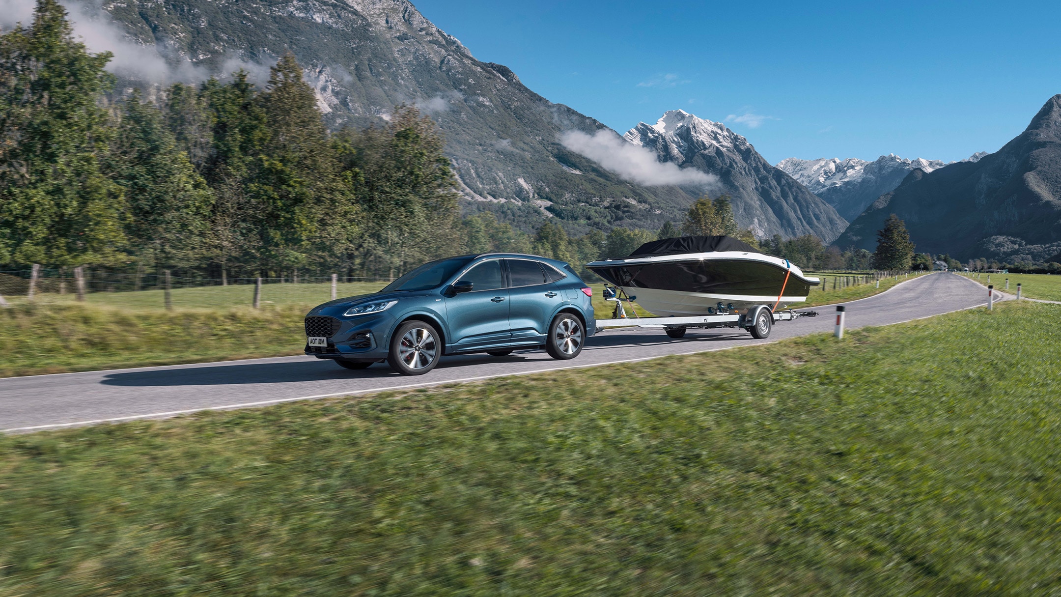 Un véhicule Ford roule avec un bateau transporté en remorque dans un paysage de montagne au printemps 