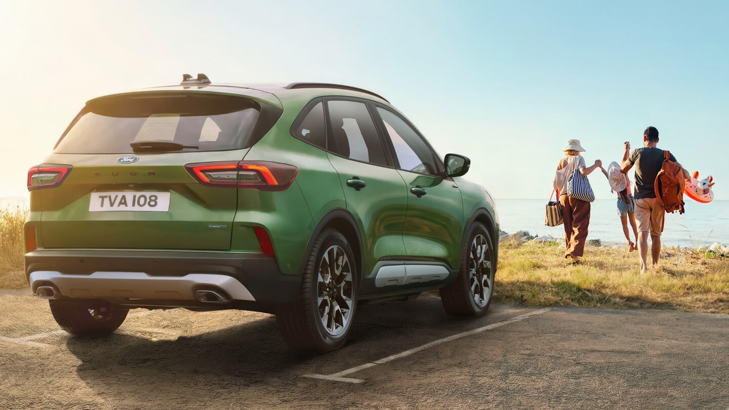 Un SUV vert garé tandis qu'une famille marche vers l'océan  avec du matériel de plage.