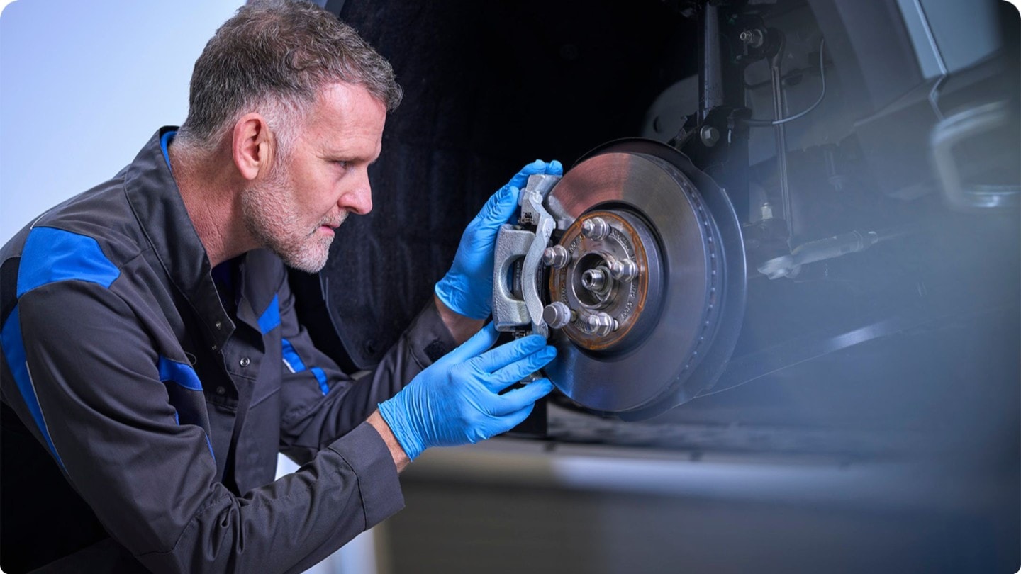 Un mécanicien portant des gants bleus inspecte l’étrier  et le disque de frein d’une voiture.
