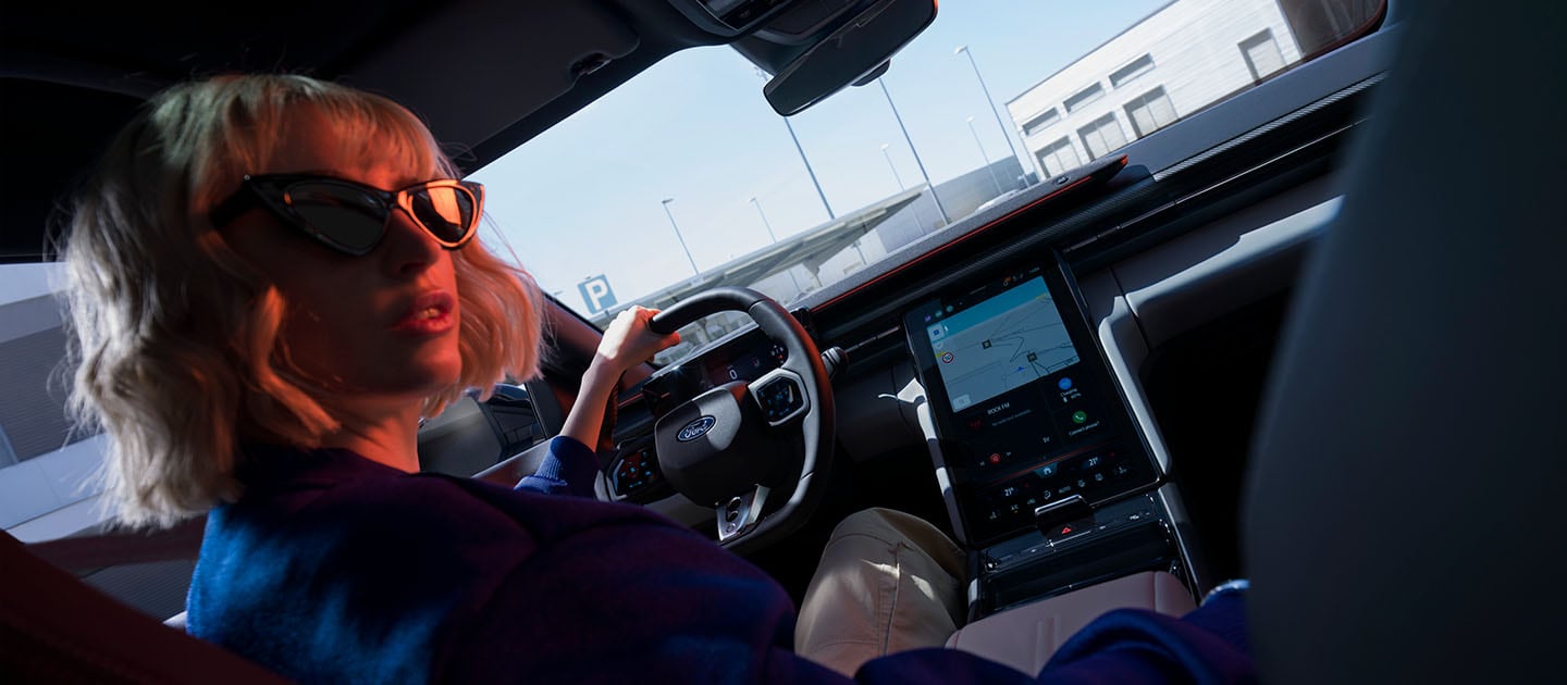 Une femme est assise au volant d'une Ford Capri électrique, avec grand écran tactile SYNC Move de 14,6 pouces.