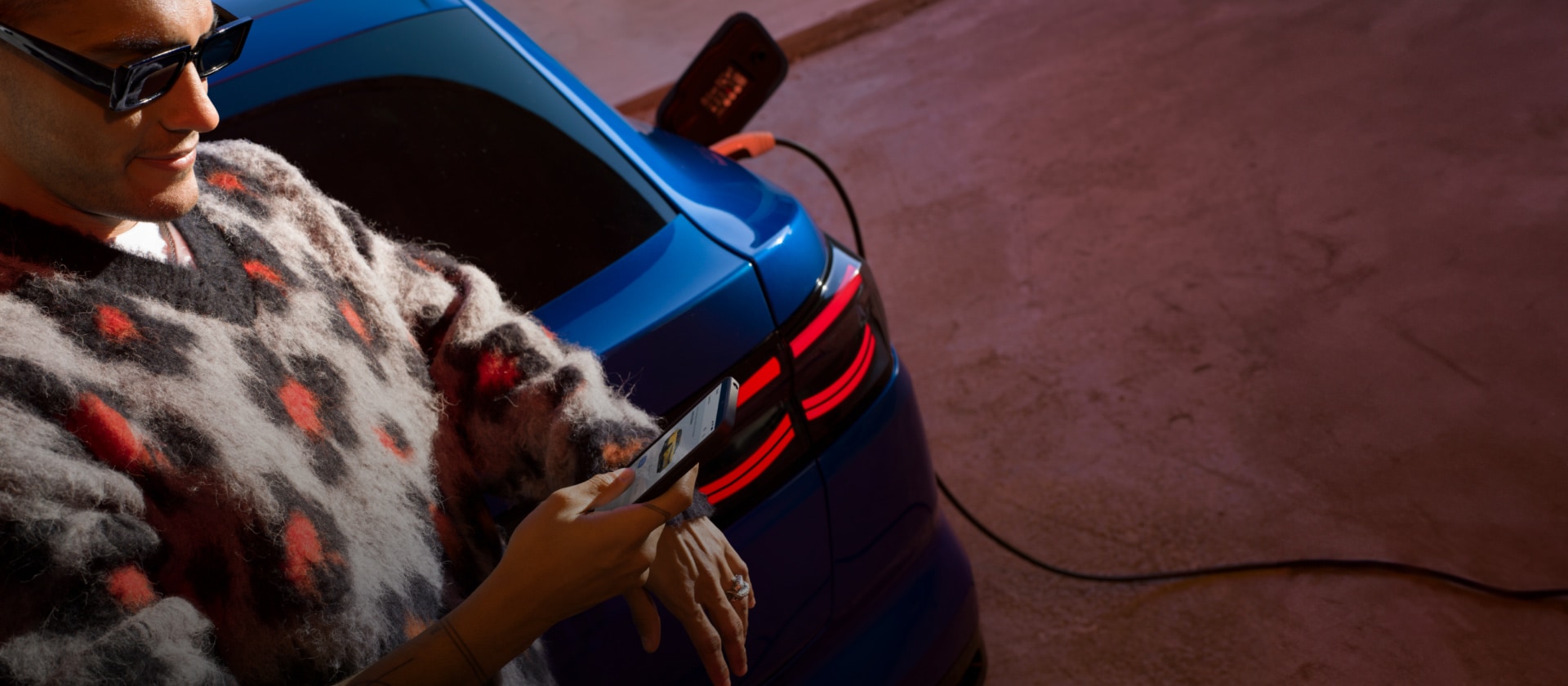 Une personne rechargeant une Ford Capri bleue à une station de recharge publique. 