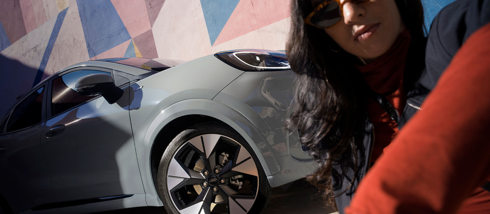 Une personne assise à côté d'une voiture hybride légère Ford Puma de couleur gris. 