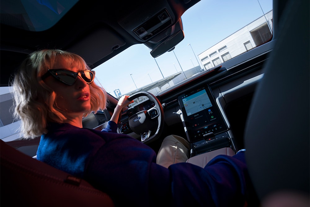 Une femme est assise au volant d'une Ford Capri électrique, avec grand écran tactile SYNC Move de 14,6 pouces.