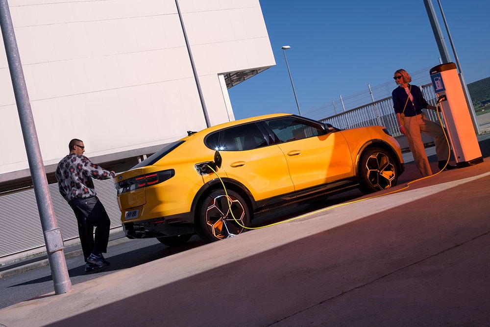 Personnes rechargeant une Ford Capri électrique jaune à une station de recharge publique. 