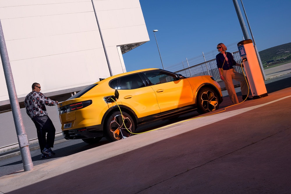 Des personnes rechargent une Ford Capri jaune à une station de recharge publique. 