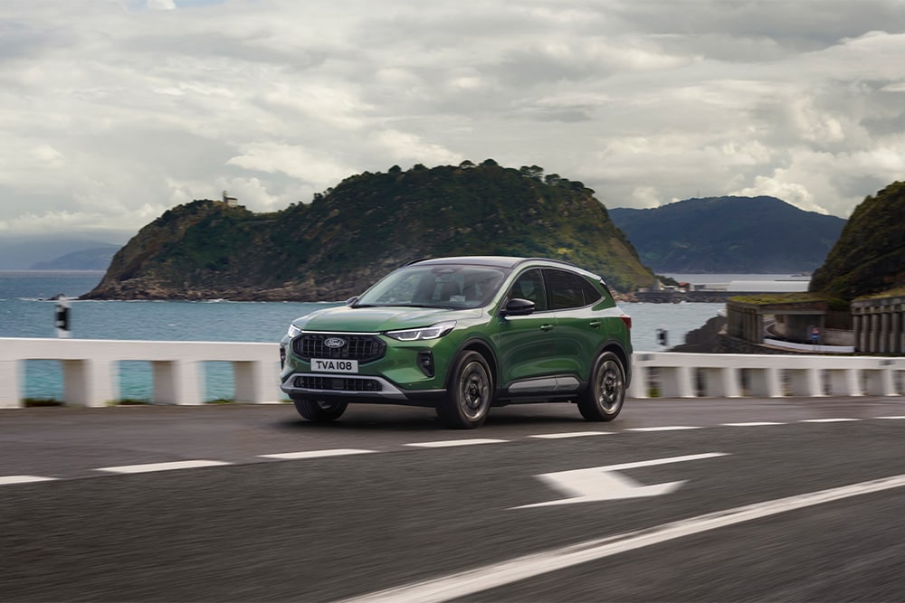 Une voiture hybride rechargeable Ford Kuga vert roulant le long d'une route. 