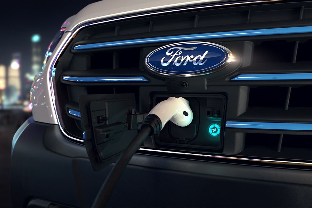 Gros plan d'une borne de recharge pour  Ford E-Transit et du badge Ford ovale bleu sur la calandre. 