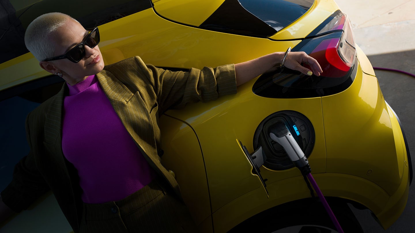 Une femme s'appuyant sur une Ford Capri électrique jaune connectée à un chargeur.