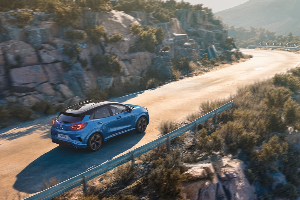 Un Puma Gen-E bleu roulant sur une route de montagne sinueuse.