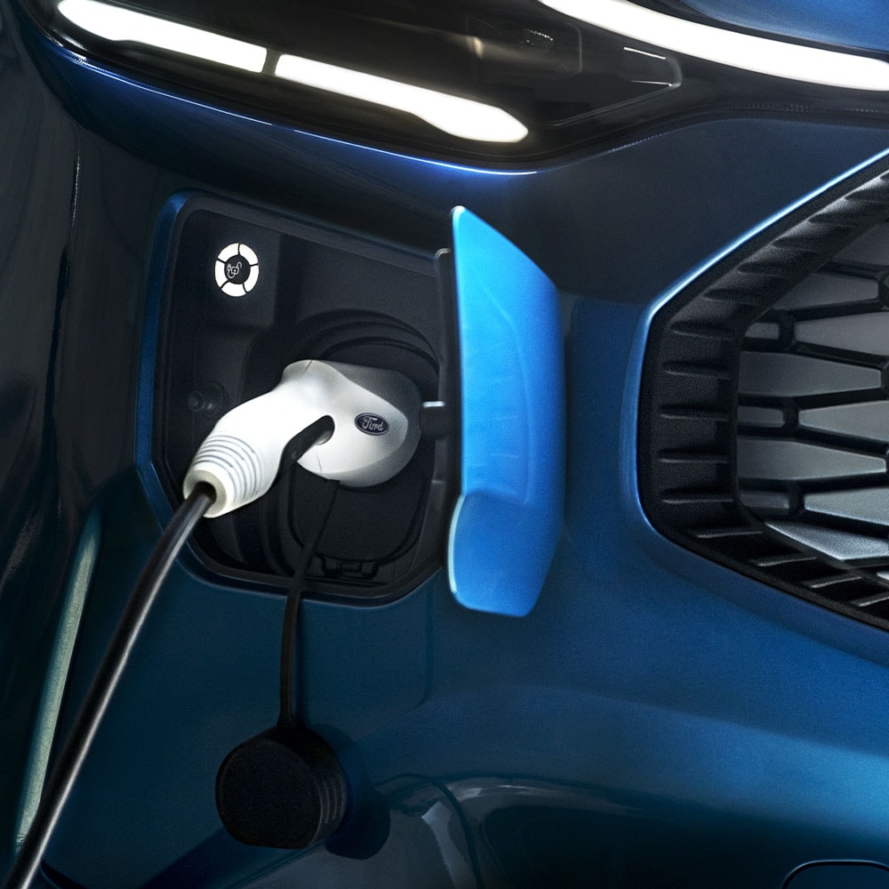 Un port de recharge pour voiture électrique avec un chargeur de VE connecté et un véhicule Ford bleu en arrière-plan.