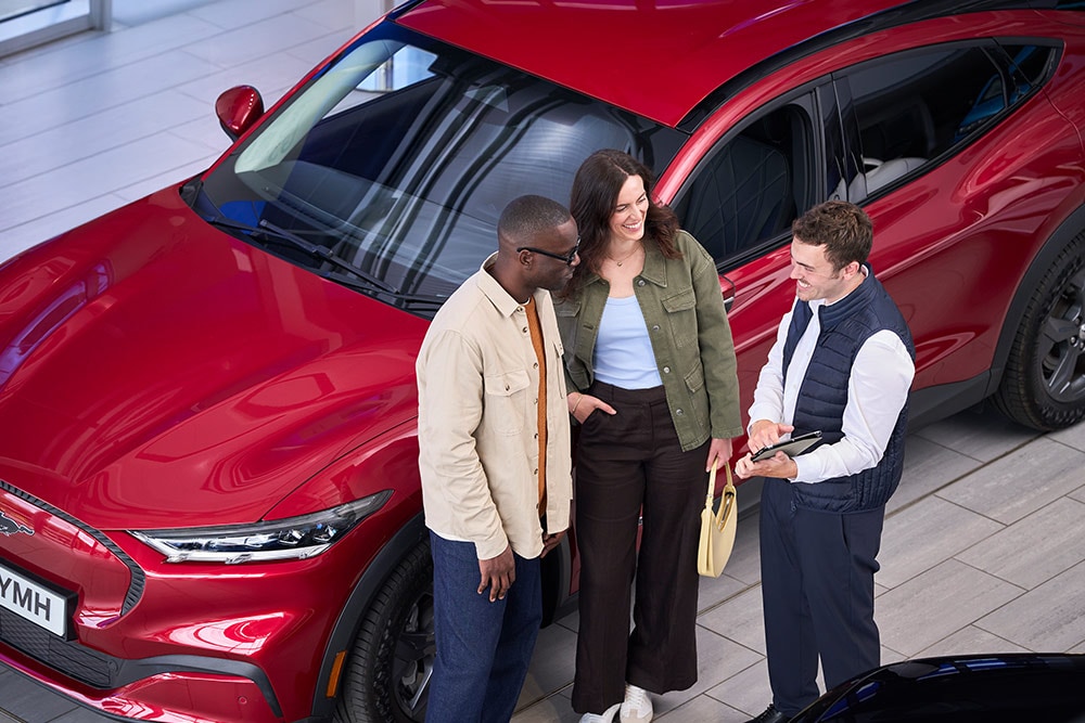 Un couple et un vendeur discutent d'une Ford Mustang Mach-E rouge dans un showroom.