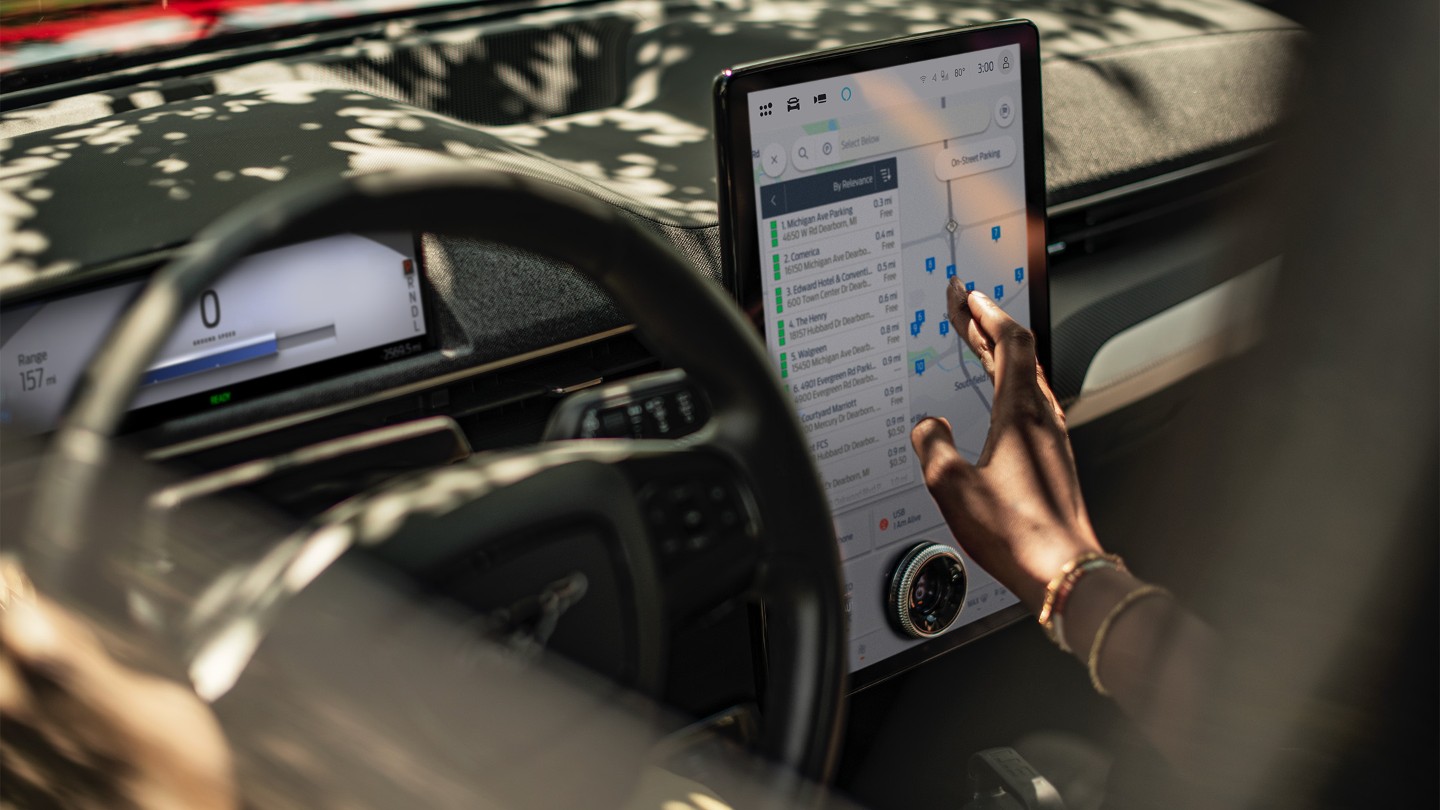 Gros plan d’une femme assise dans une Ford Mustang Mach-E, interagissant avec le grand écran tactile SYNC.