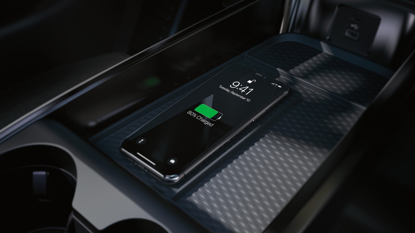Gros plan du socle de recharge sans fil dans la console centrale, avec un iPhone en cours de chargement.