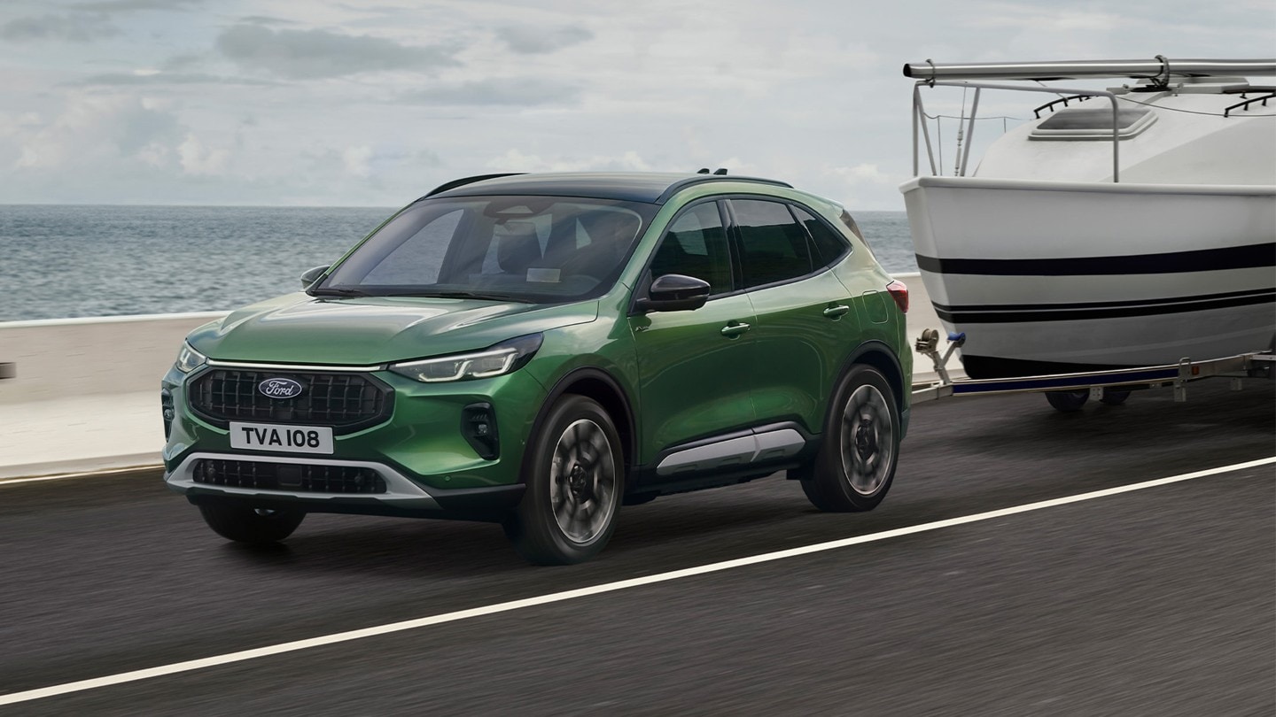 Ford Kuga verte tractant un petit bateau le long d’une route côtière.