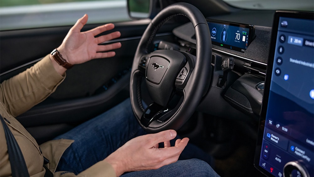 Un homme assis dans une Ford Mustang Mach-E, les mains éloignées du volant, illustrant la technologie BlueCruise.