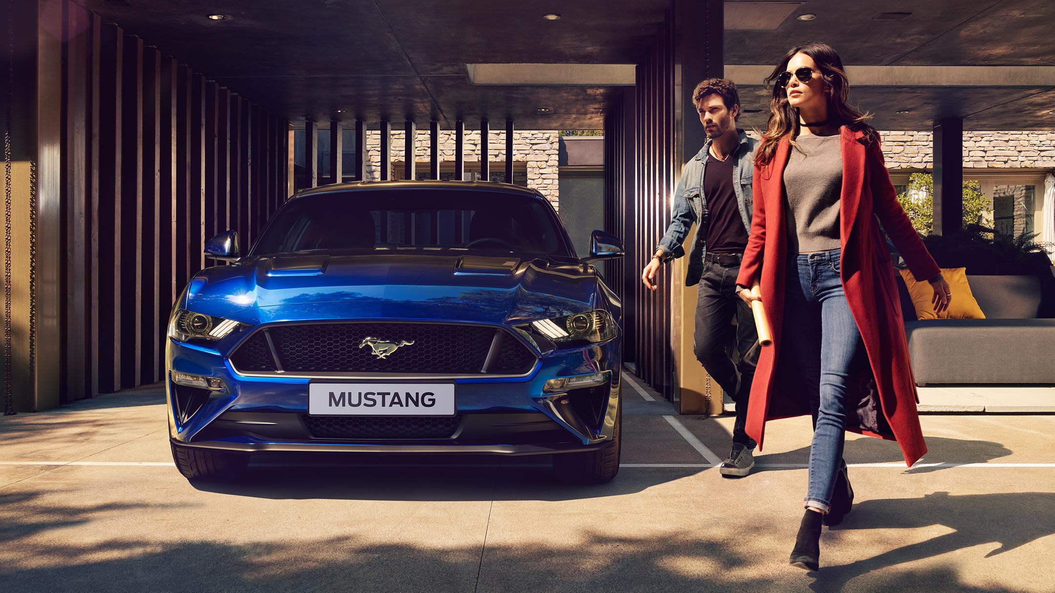 Un couple marchant à côté d’une Ford Mustang bleue.