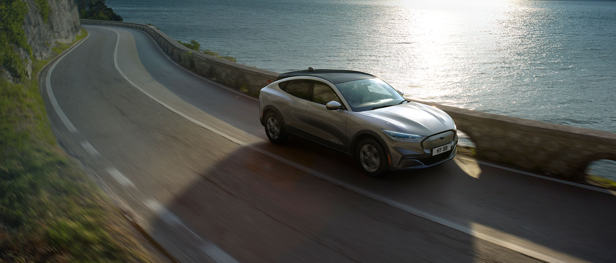 Nouvelle Ford Mustang Mach-E roulant sur une route ensoleillée près de la mer