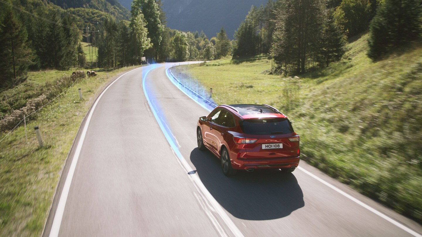 Le Ford Kuga rouge roulant sur la route en montrant le système d’aide au maintien dans la voie