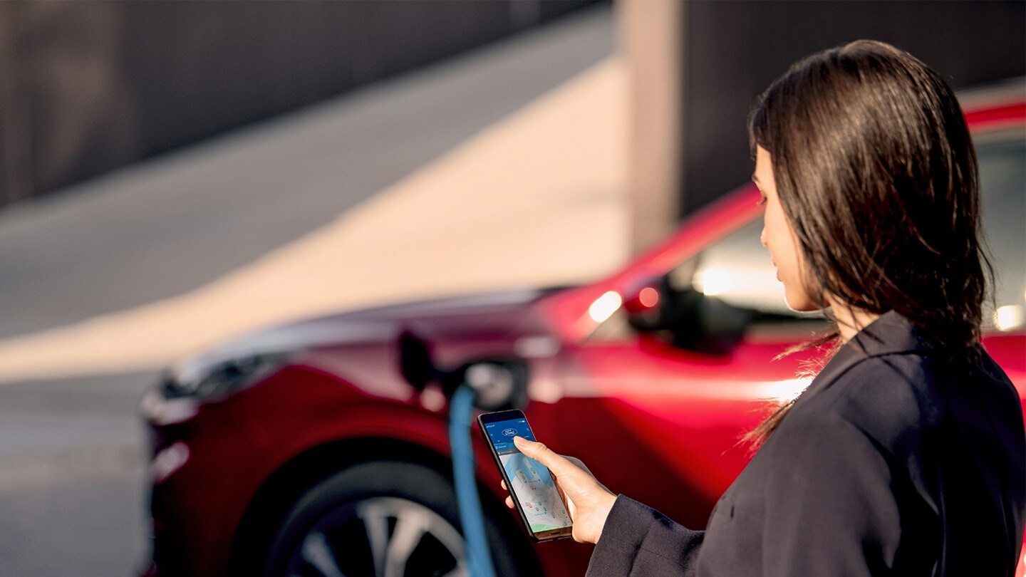 Femme consultant son téléphone mobile pendant le chargement de son Ford Kuga