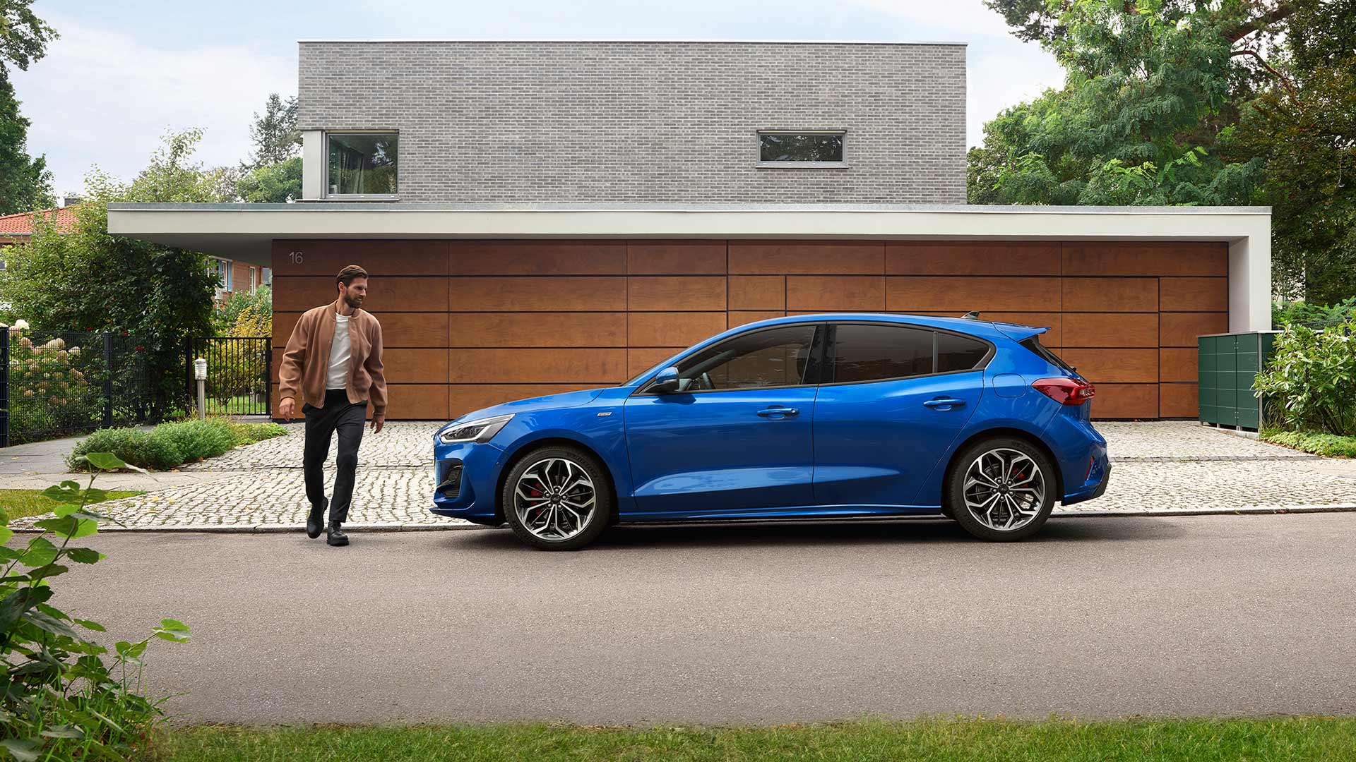 Un homme s'approche d'une Ford Focus bleue garée devant une maison