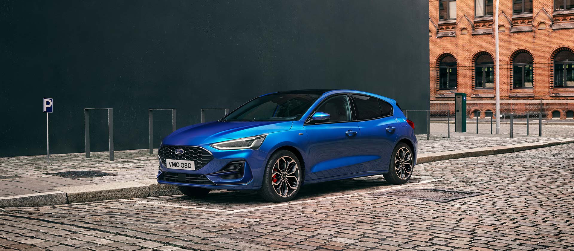 Une Ford Focus bleue à hayon garée dans une rue pavée en milieu urbain.