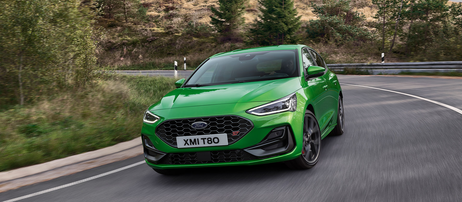 Une Ford Focus ST de couleur vert moyen au détour d'un virage sur une route pittoresque.