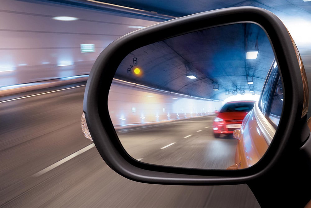 Gros plan sur le rétroviseur latéral d'un tunnel, montrant une voiture rouge s'approchant dans l'angle mort du conducteur.