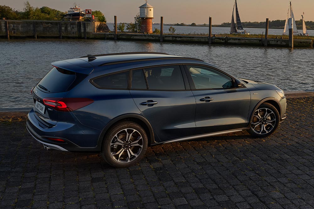 Une Ford Focus Active Estate bleu foncé garée près d'un plan d'eau au crépuscule.
