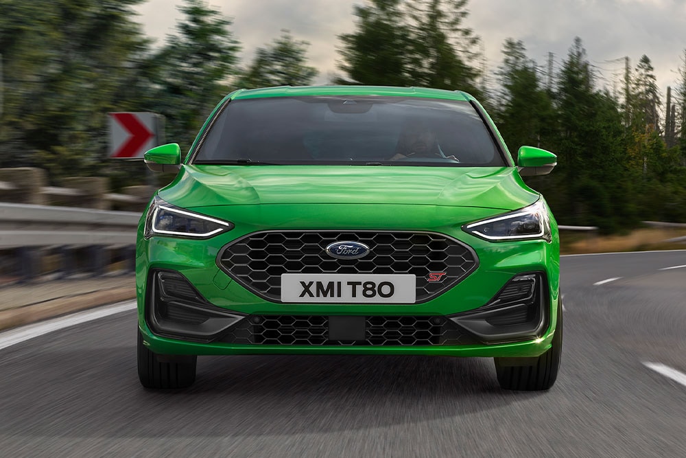 L'avant d'une Ford Focus ST de couleur vert moyen prenant un virage, avec des arbres flous en arrière-plan.