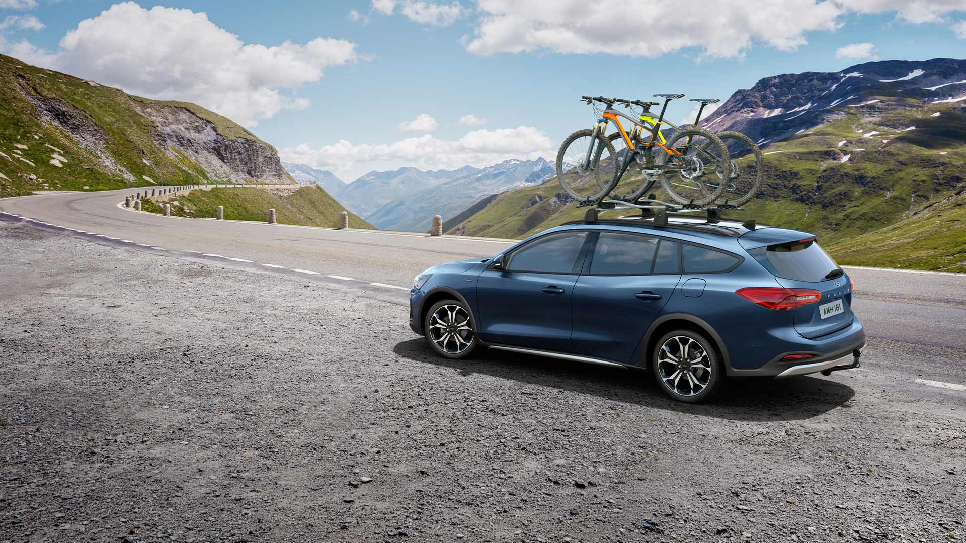 Ford Focus bleue transportant des vélos sur son toit et circulant le long d’une route de montagne pittoresque.