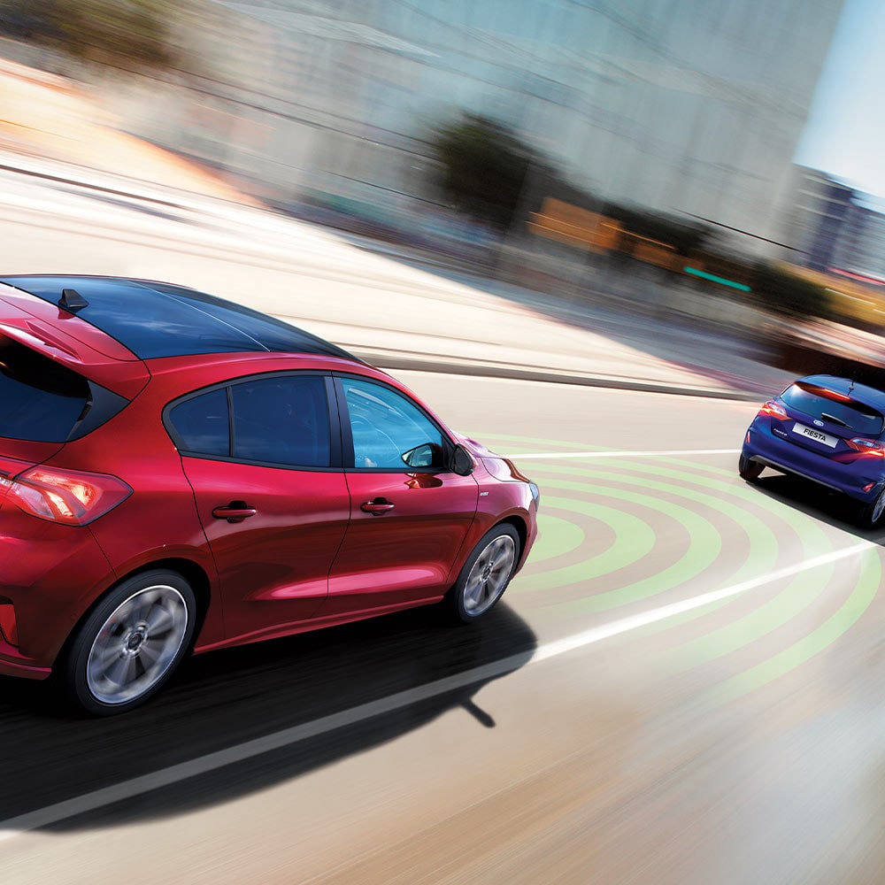 Un graphique montrant une Ford Focus rouge utilisant des capteurs, indiqués par des lignes bleues, pour détecter la voiture qui la précède dans le cadre du système de freinage d'urgence.