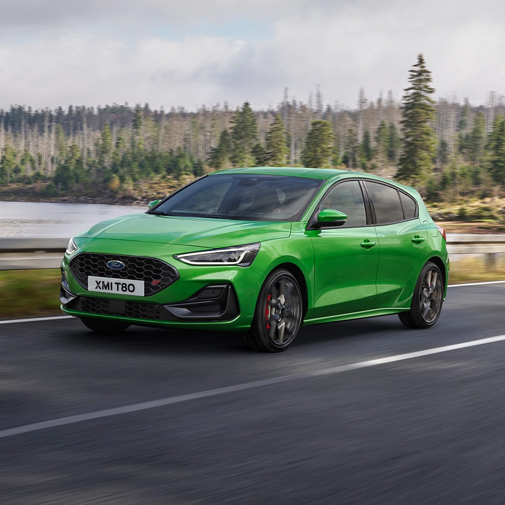 Une Ford Focus ST vert foncé roule sur une route sinueuse entourée d'arbres.