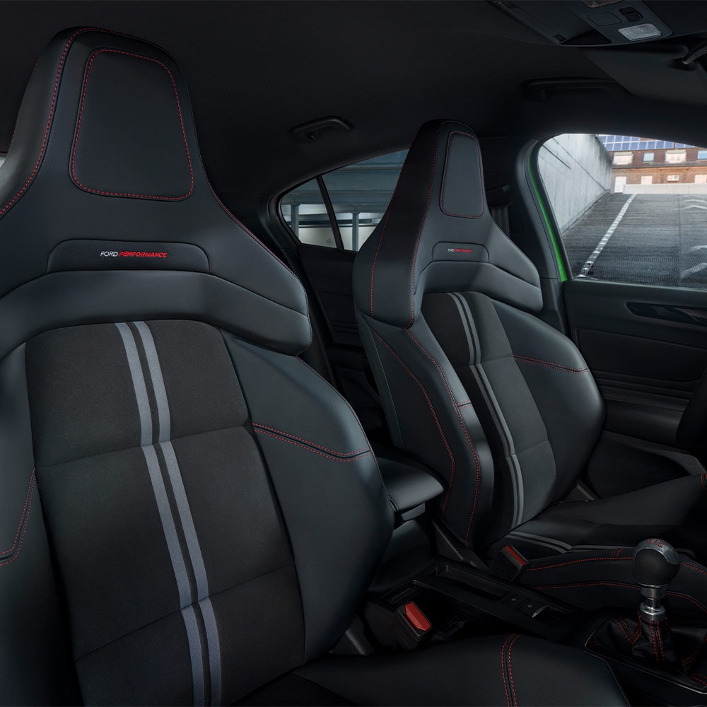 Gros plan sur les sièges sport de la Ford Focus ST, dotés d'une sellerie sombre avec des surpiqûres contrastées rouges.