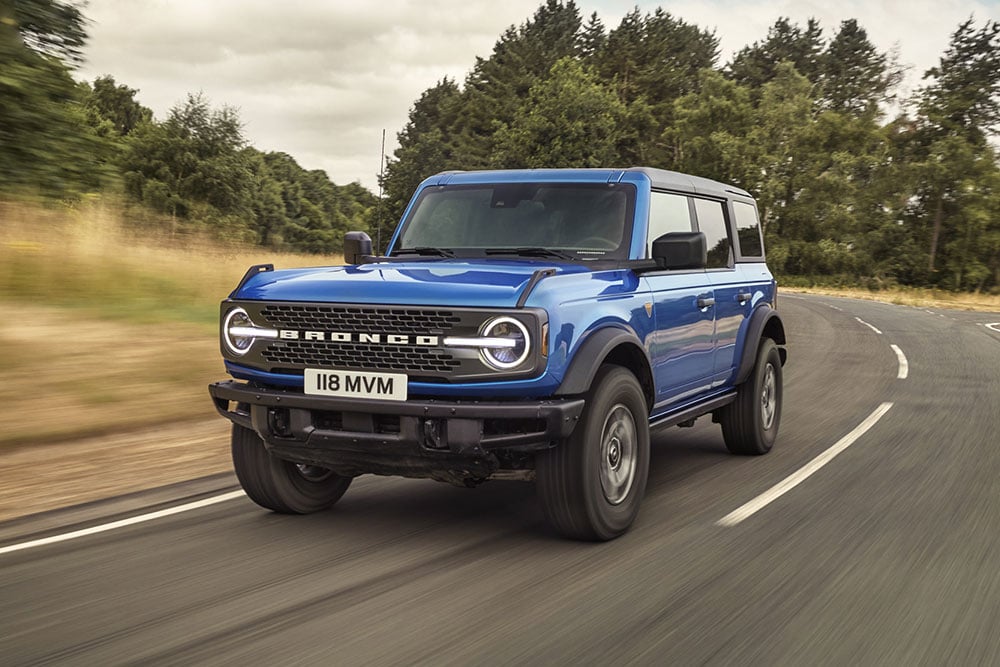 Front view of the new Ford Bronco in blue driving on a country round.