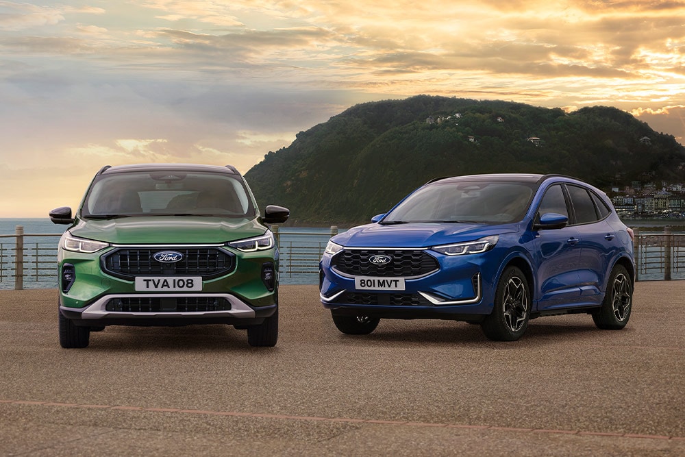Une Ford Kuga Active verte et une Ford Kuga ST Line bleue garées côte à côte dans un parking côtier. 
