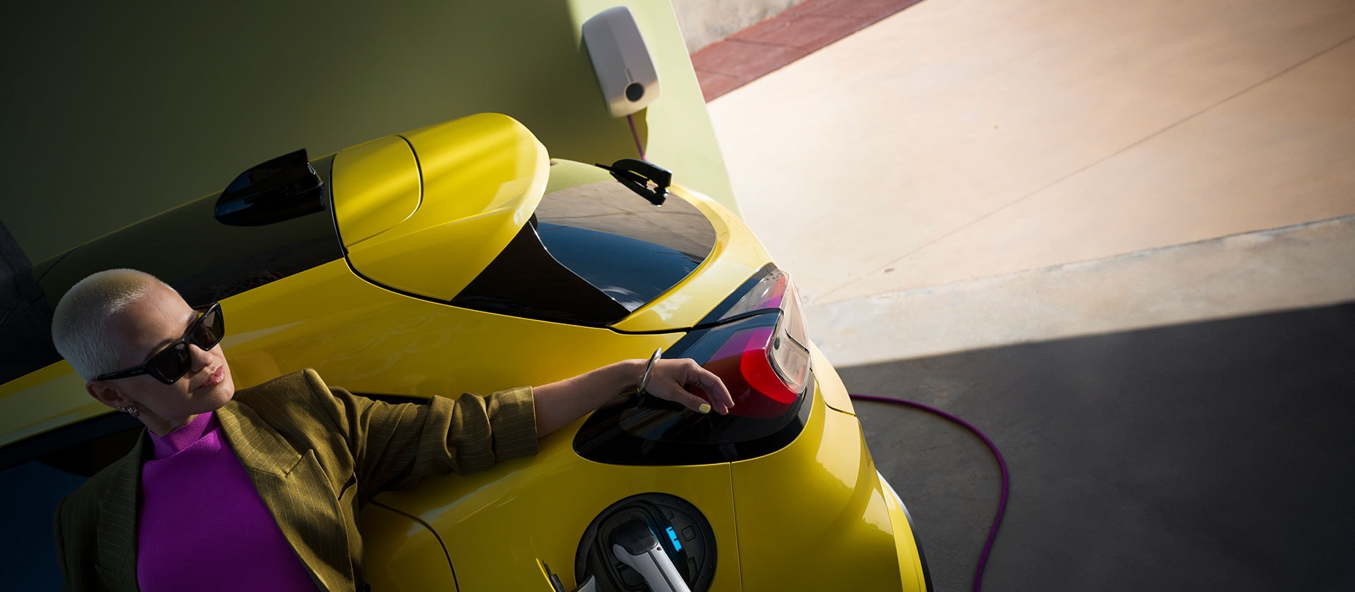 Un gros plan de l’arrière d’une Ford Puma Gen-E® électrique jaune, branchée à une borne de recharge murale à domicile.