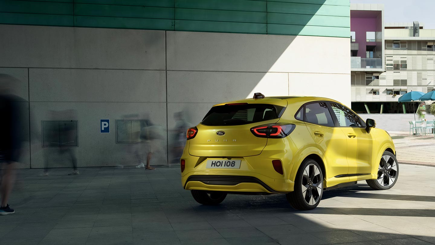 L’angle arrière d’une Ford Puma Gen-E® électrique jaune stationnée sous un pont.