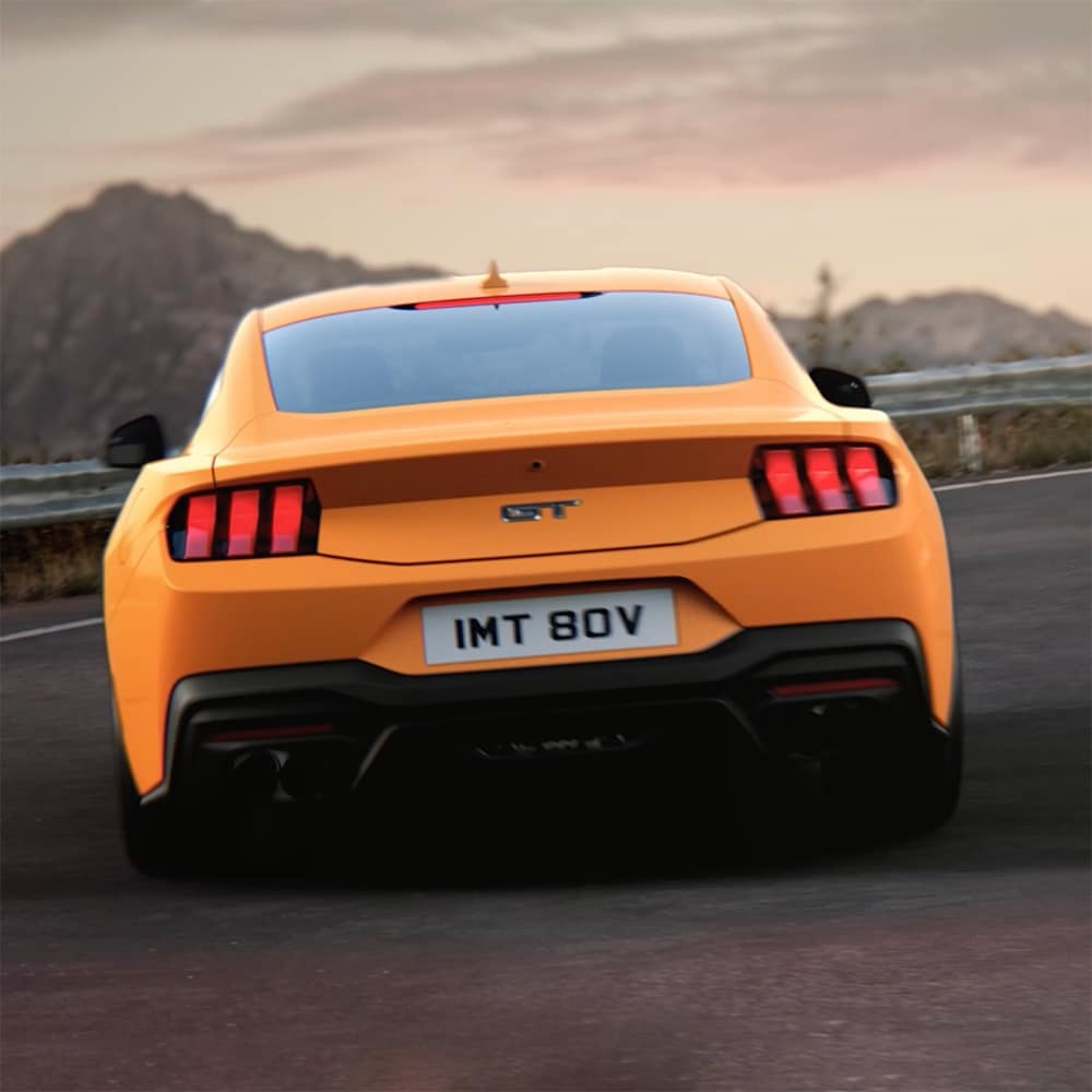 L’arrière d’une Ford Mustang GT Fastback en peinture Orange Fury, négociant un virage serré sur une route de campagne