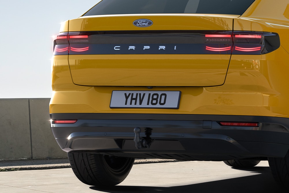 Vue arrière d’une Ford Capri® jaune circulant sur une route urbaine.