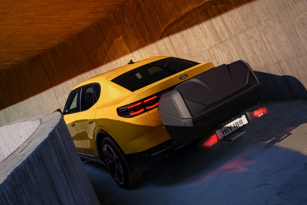 Vue arrière d’une Ford Capri de couleur jaune stationnée dans un environnement moderne en béton avec coffre de rangement monté sur l’attelage.