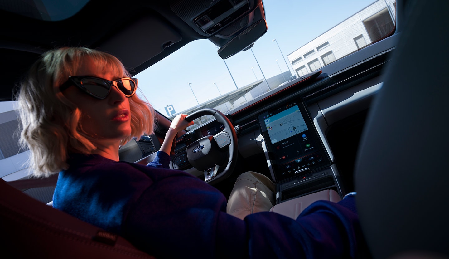 Une femme est assise sur le siège conducteur d’une Ford Capri® garée, avec vue sur le volant et le grand écran tactile SYNC® Move.