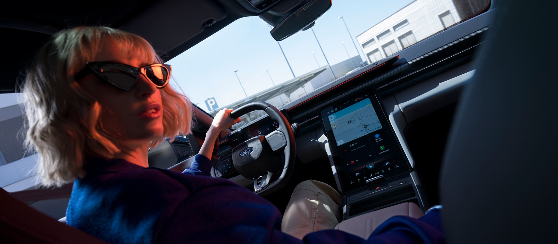 Une femme est assise sur le siège conducteur d’une Ford Capri® garée, avec vue sur le volant et le grand écran tactile SYNC® Move.