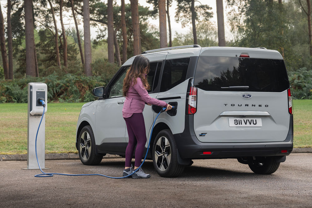 Une personne branche un Ford E-Tourneo Courier gris à une borne de recharge extérieure