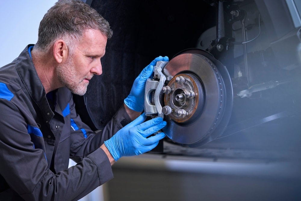 Un mécanicien portant des gants bleus inspecte l’étrier  et le disque de frein d’une voiture.