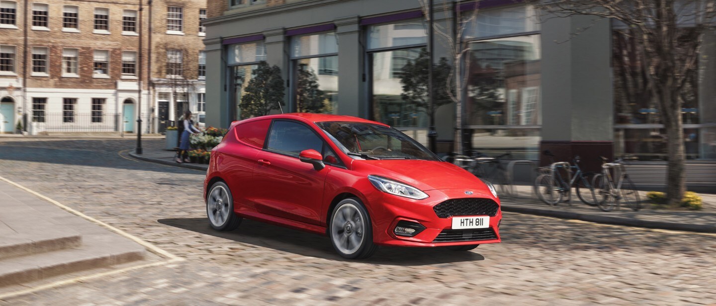 Ford Fiesta Van driving in city next to shops Ford Fiesta Van driving in city next to shops