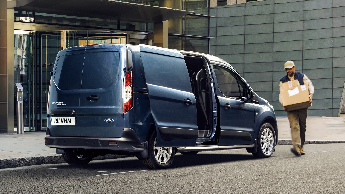 Le Ford Transit Connect garé à proximité d’un bâtiment avec sa porte latérale ouverte et un homme portant un carton.