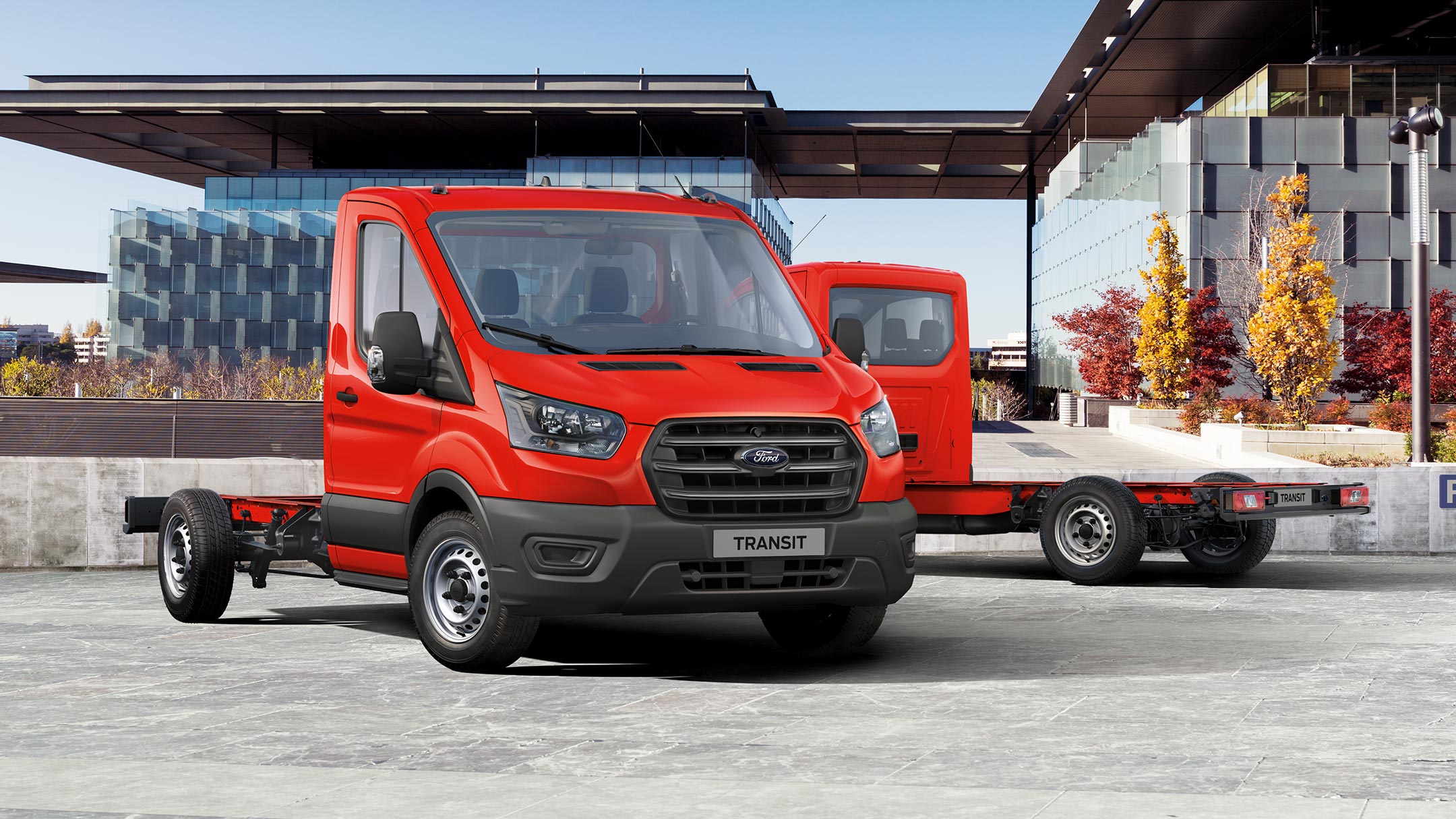 Vue latérale du Ford Transit Châssis Cabine rouge devant un batiment en construction.