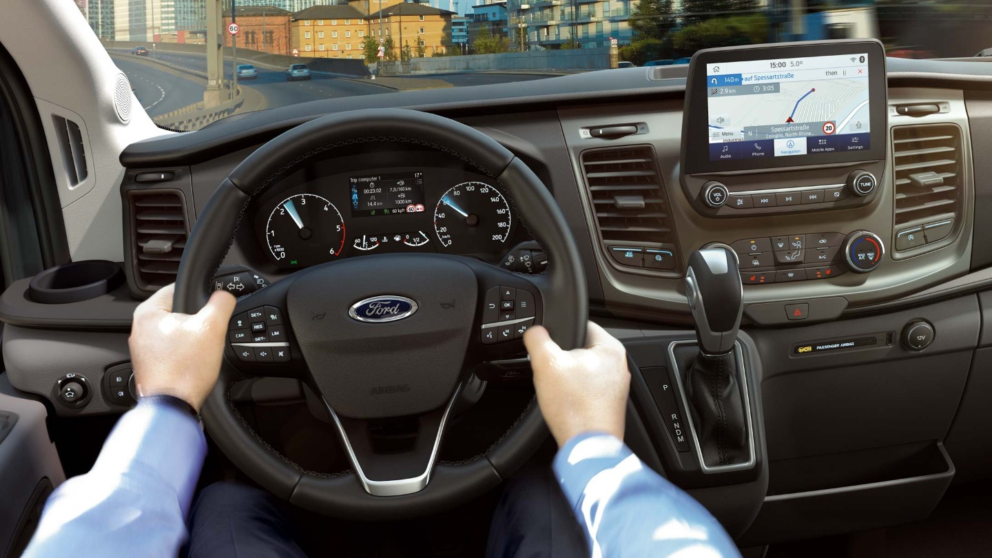 Vue intérieure du Ford Transit avec le volant, l’écran SYNC 3 et son conducteur.